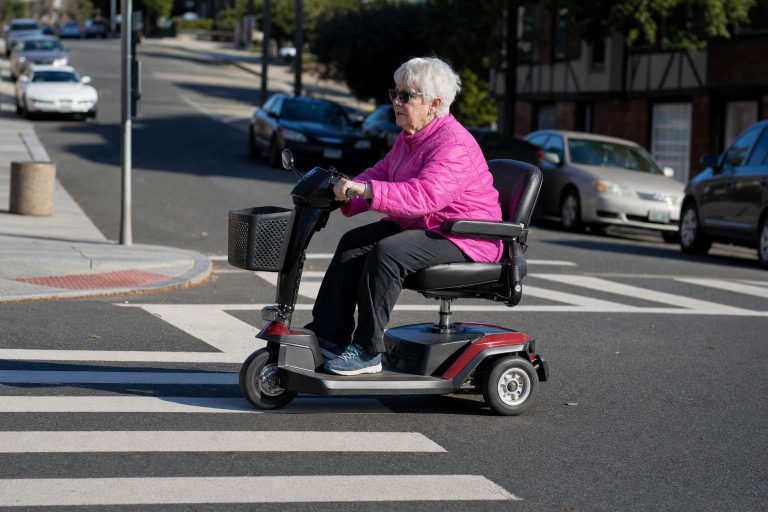An older adult riding a mobility scooter across a crosswalk.
