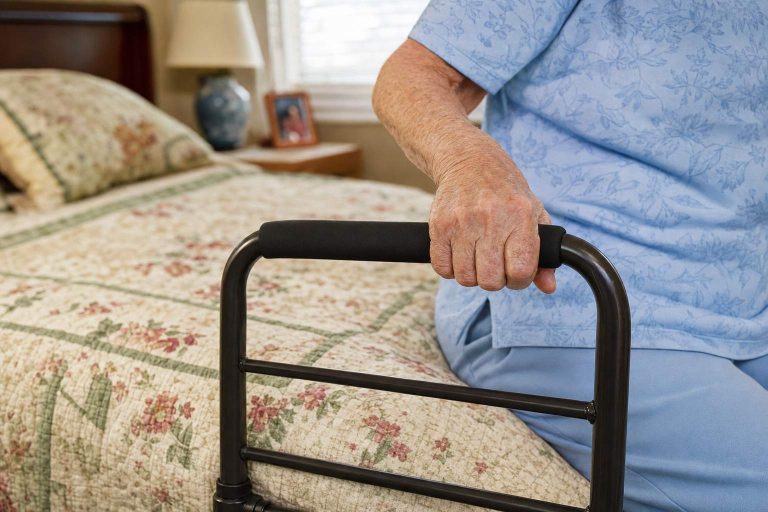 An older adult's hand gripping a bedside assist rail next to a neatly made bed
