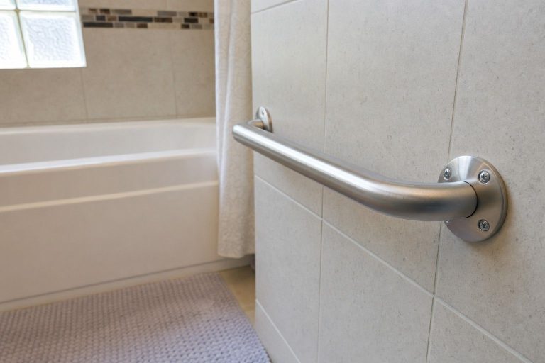 A stainless steel grab bar securely mounted on the tiled wall beside a bathtub