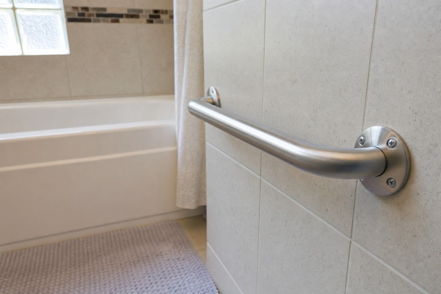 A stainless steel grab bar securely mounted on the tiled wall beside a bathtub