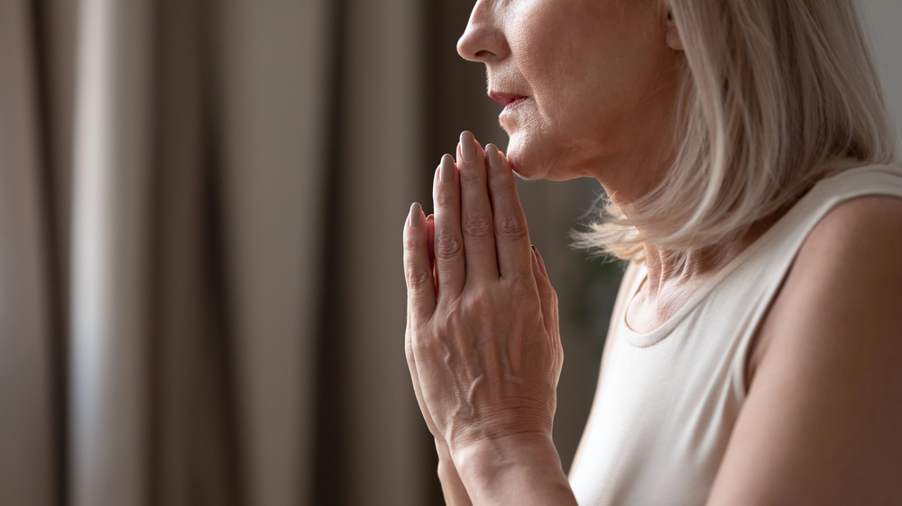 Elderly woman sitting thoughtfully at home and keeping hands together