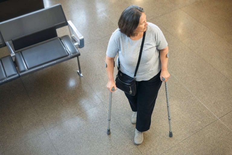 An older adult using crutches to move through an airport terminal.