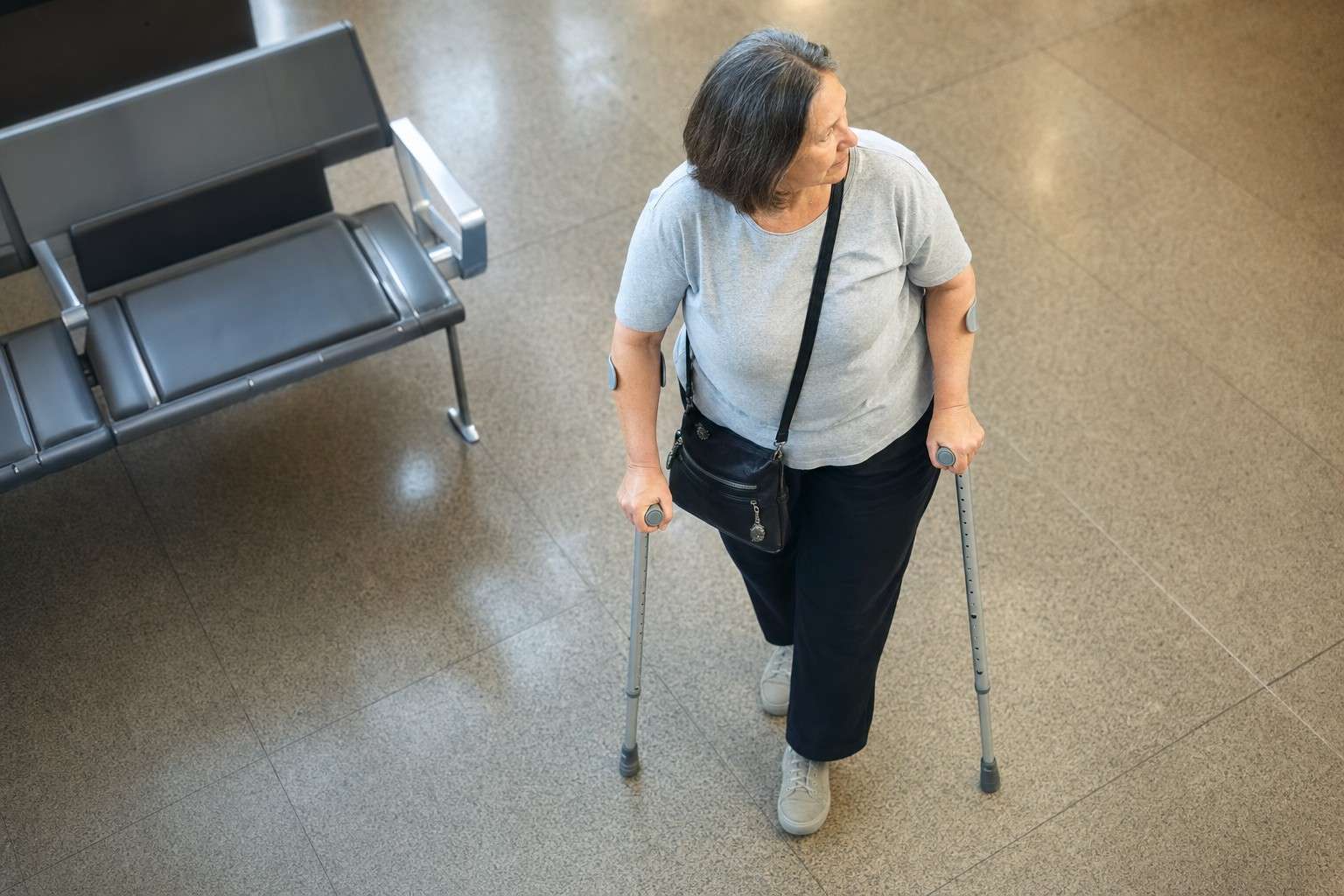 An older adult using crutches to move through an airport terminal.