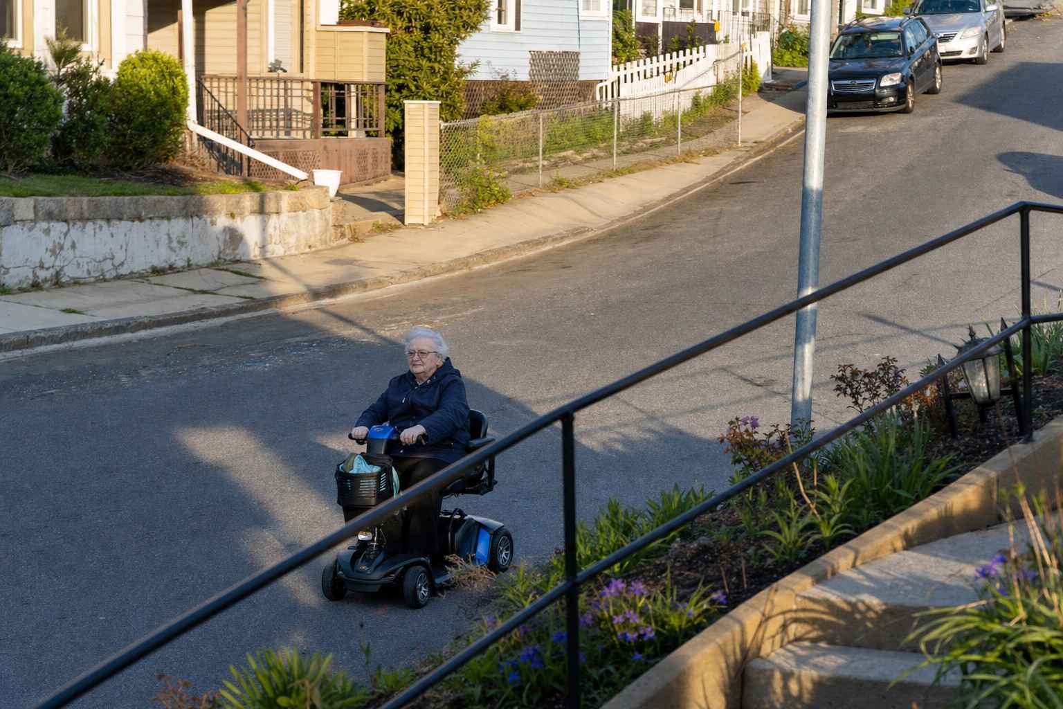 An older adult riding a mobility scooter up a sloped street.