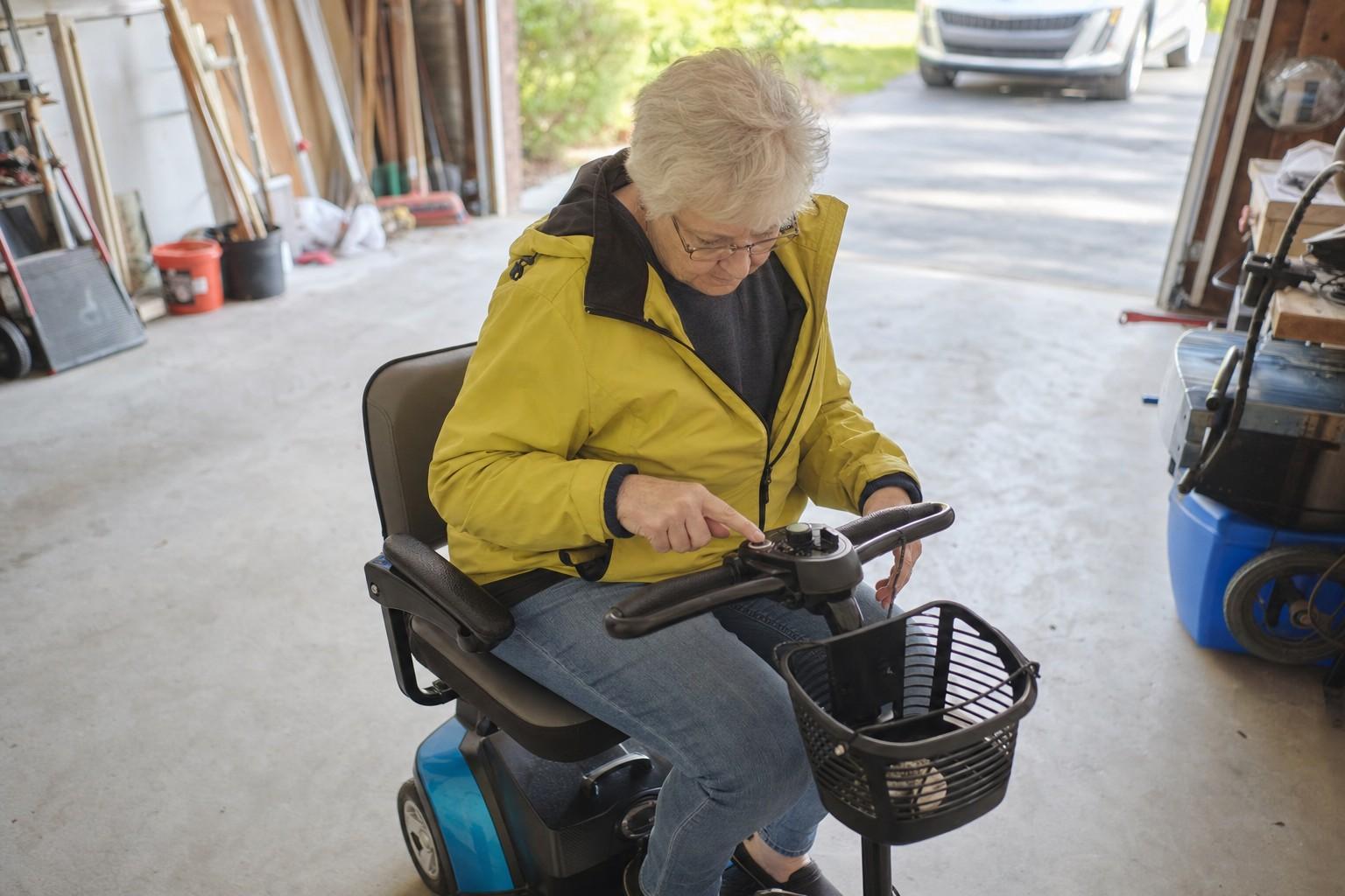 An older adult checking a stalled mobility scooter in a garage.
