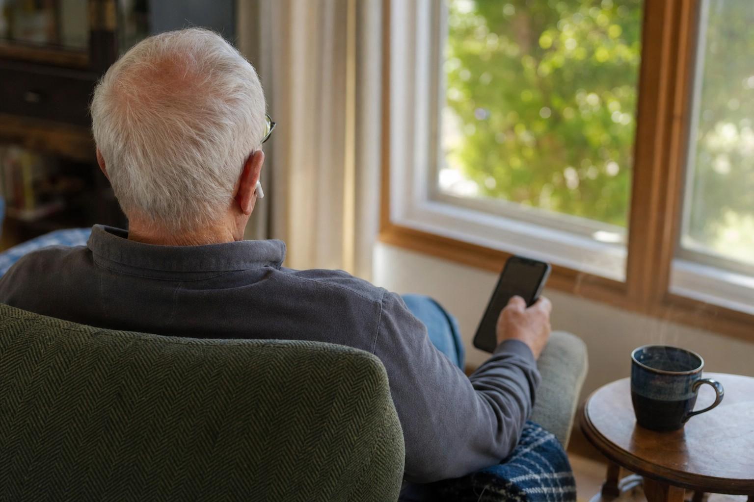 An older adult relaxing in an armchair listening with earbuds.